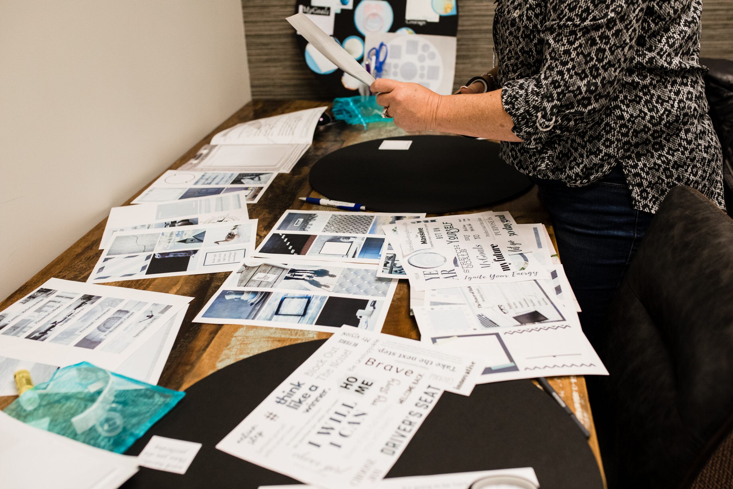woman at a vision board party with her graphics spread out on a table where she is assembling her board