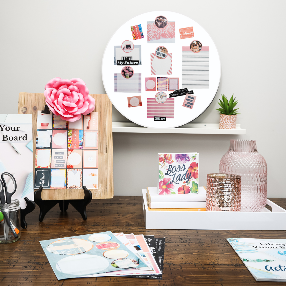 product photo of a vision board kit that contains foam board, pink graphics and images, goal setting workbook all displayed on wood table